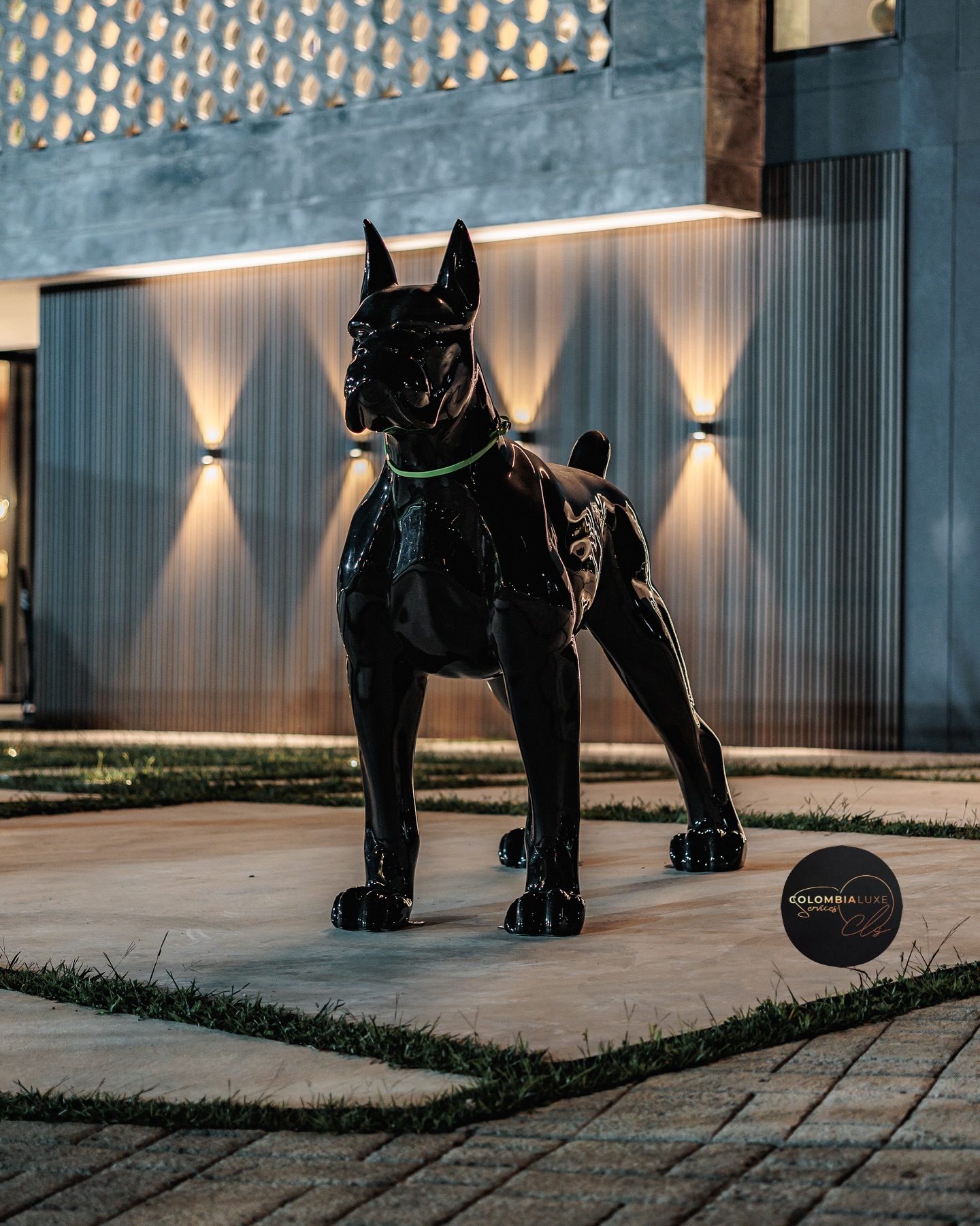A black dog sculpture lit at night in front of a stone wall
