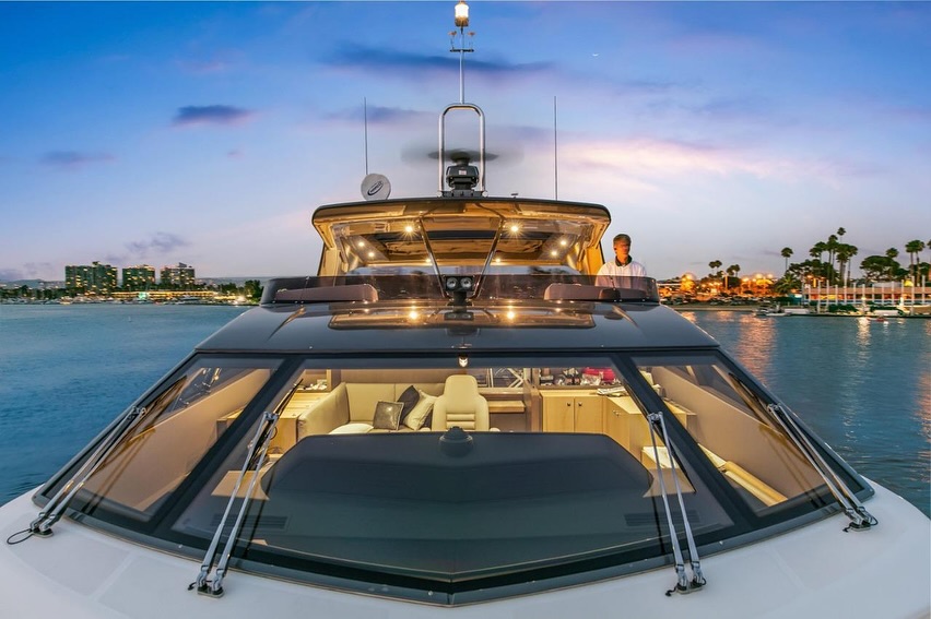 Bow of a large yacht at dusk, lit cabin and city lights across the water
